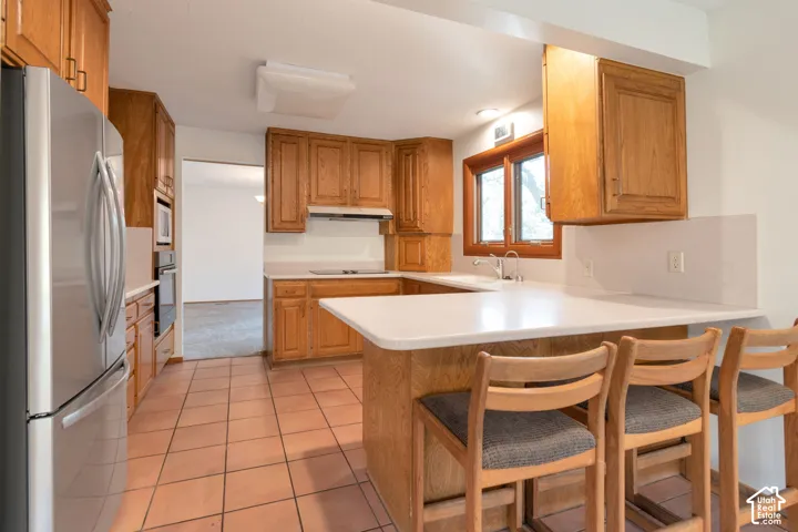 U-shaped kitchen with wood cabinetry, light-toned countertops, and terracotta tile flooring