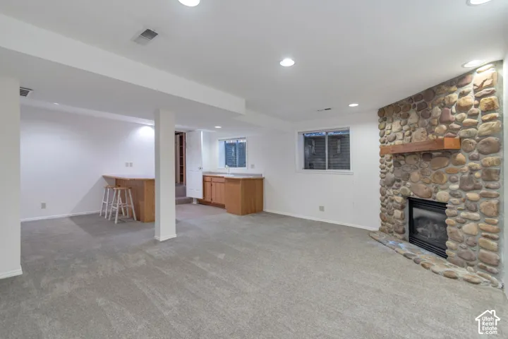 Stone-clad fireplace with a wood mantle, recessed lighting, wall-to-wall carpeting, and wood-finish cabinetry