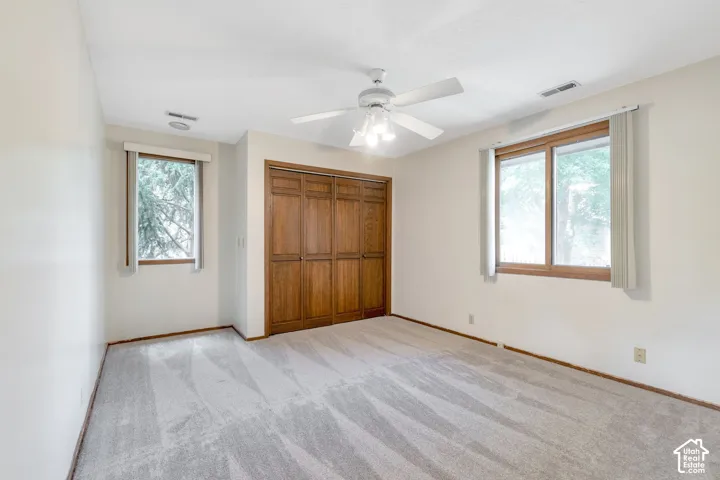 Spacious bedroom featuring gleaming wood-finish flooring, abundant natural light from dual windows with wooden frames, ceiling fan with integrated lighting, and a substantial wood-panel closet with double doors