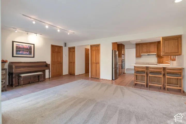 Open-concept layout featuring track lighting, wood-finish cabinetry, stainless steel appliances, and a breakfast bar