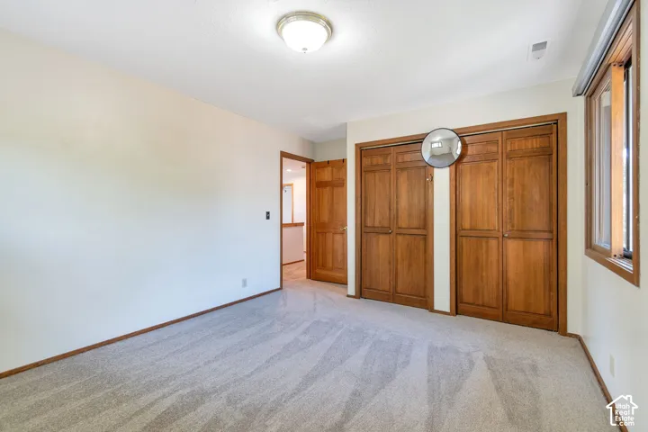 Spacious bedroom with wood-finish closet doors, neutral carpeting, and abundant natural light from multiple windows