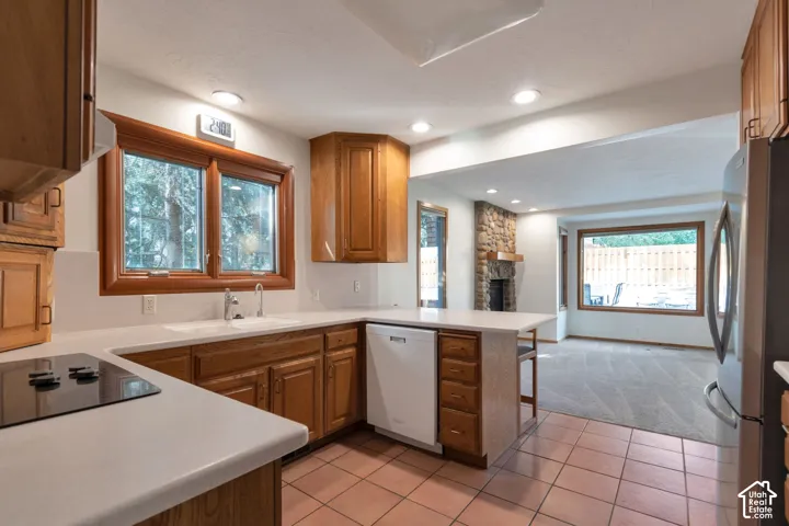 Spacious kitchen featuring warm wood cabinetry, white quartz countertops, stainless steel appliances including a refrigerator and dishwasher, and tile flooring