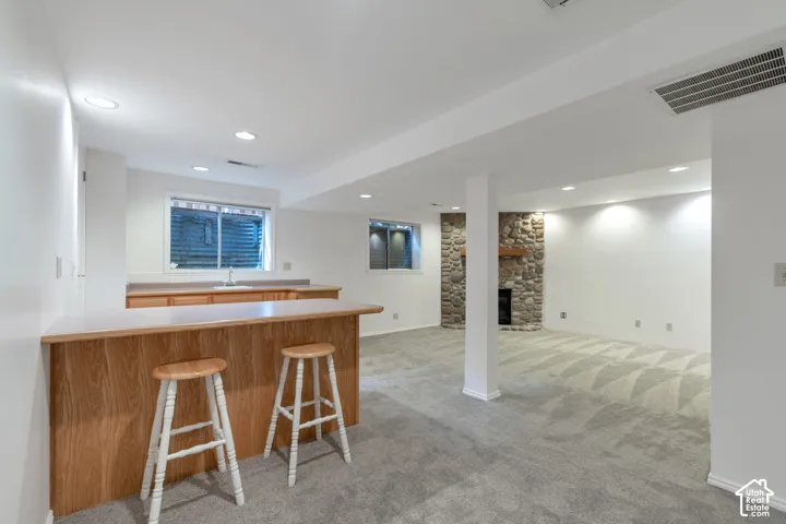 Lower level living area with a built-in wet bar, stone surround fireplace, overhead recessed lighting, and patterned carpeting