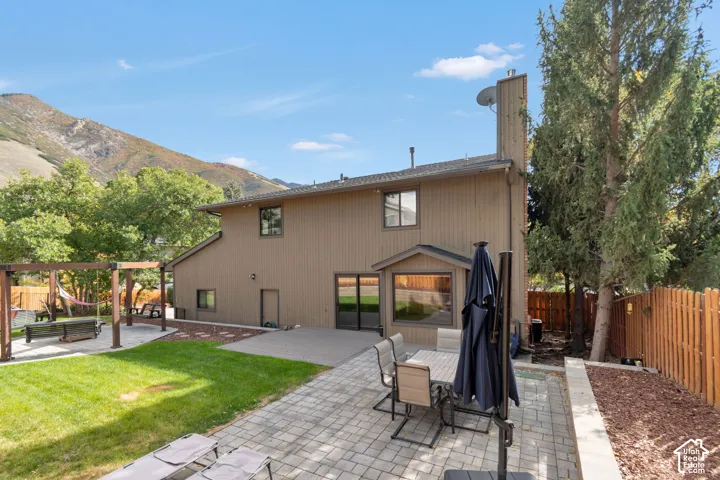 Expansive backyard featuring a manicured lawn, two distinct paved patio areas, and a wooden pergola structure