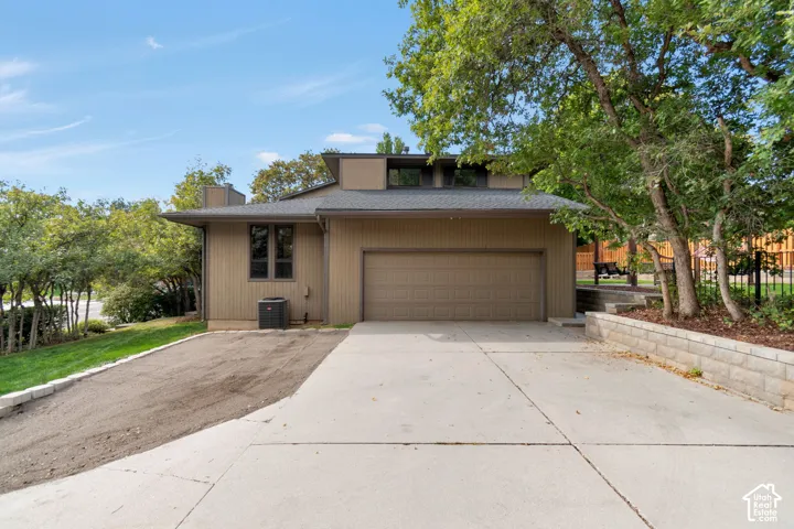 Split-level architectural style, attached garage, concrete driveway, retaining wall, mature trees