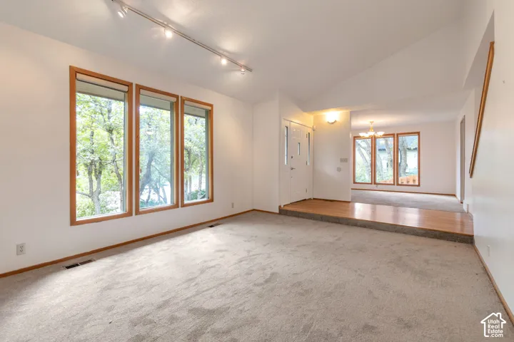 Vaulted ceiling, track lighting, light wood-finish window frames, light wood-finish flooring, and white walls