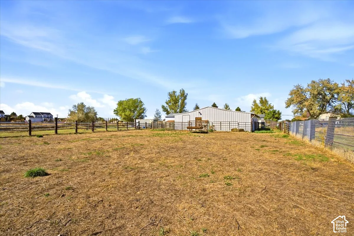 Expansive open field with a perimeter fence, mature trees, and a metal-sided utility building