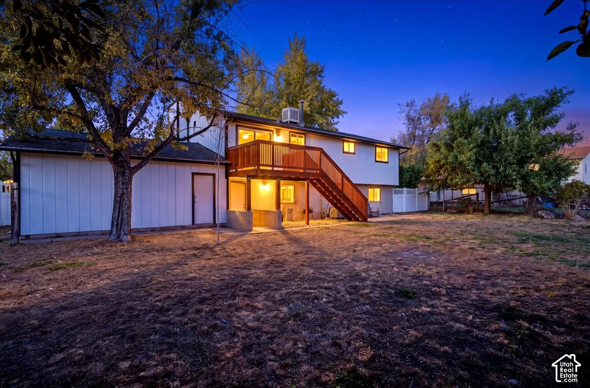 Expansive backyard with a multi-level deck featuring wood railings, a white privacy fence, and mature trees