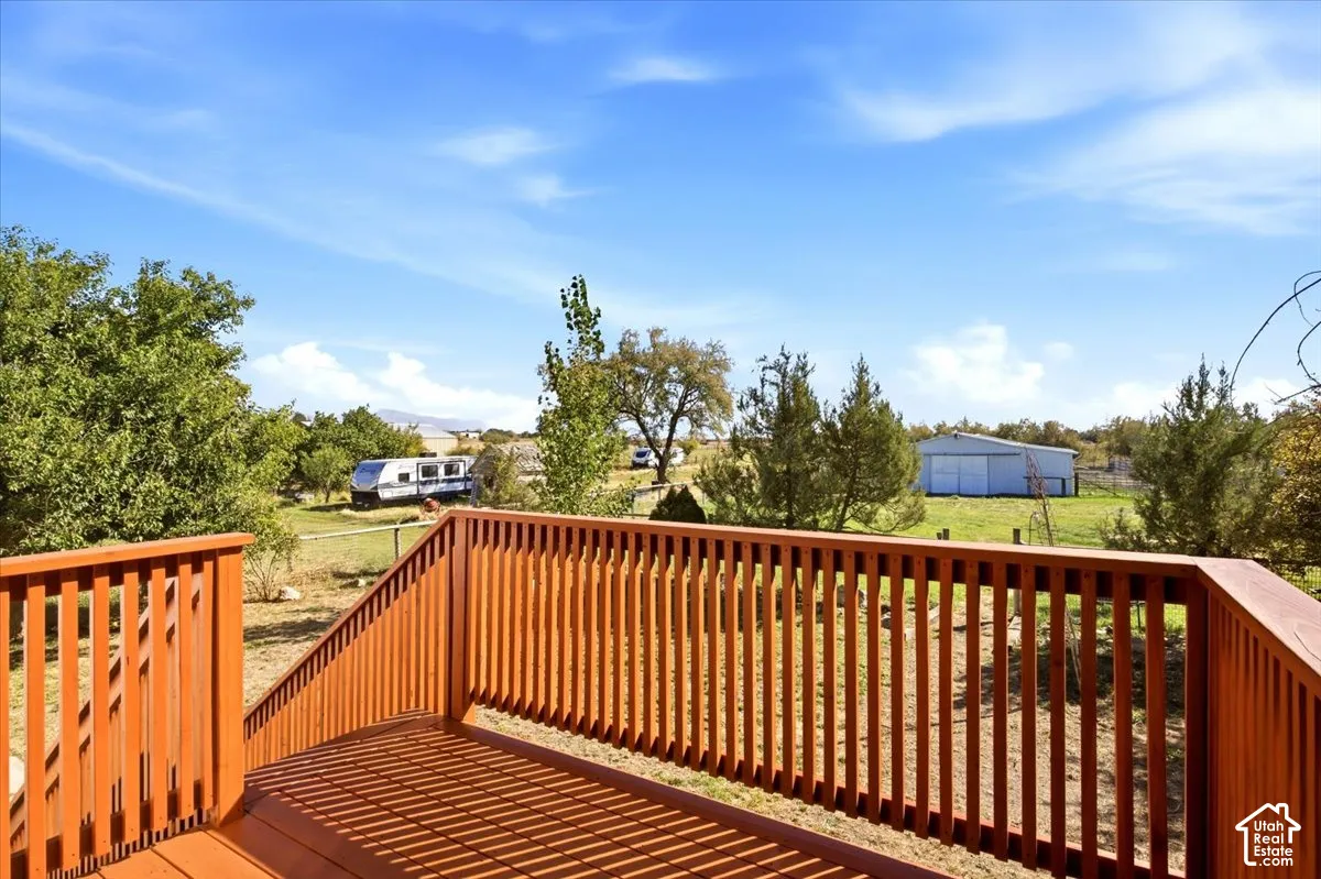 Expansive wood deck with railings overlooking a natural landscape featuring mature trees and a distant structure
