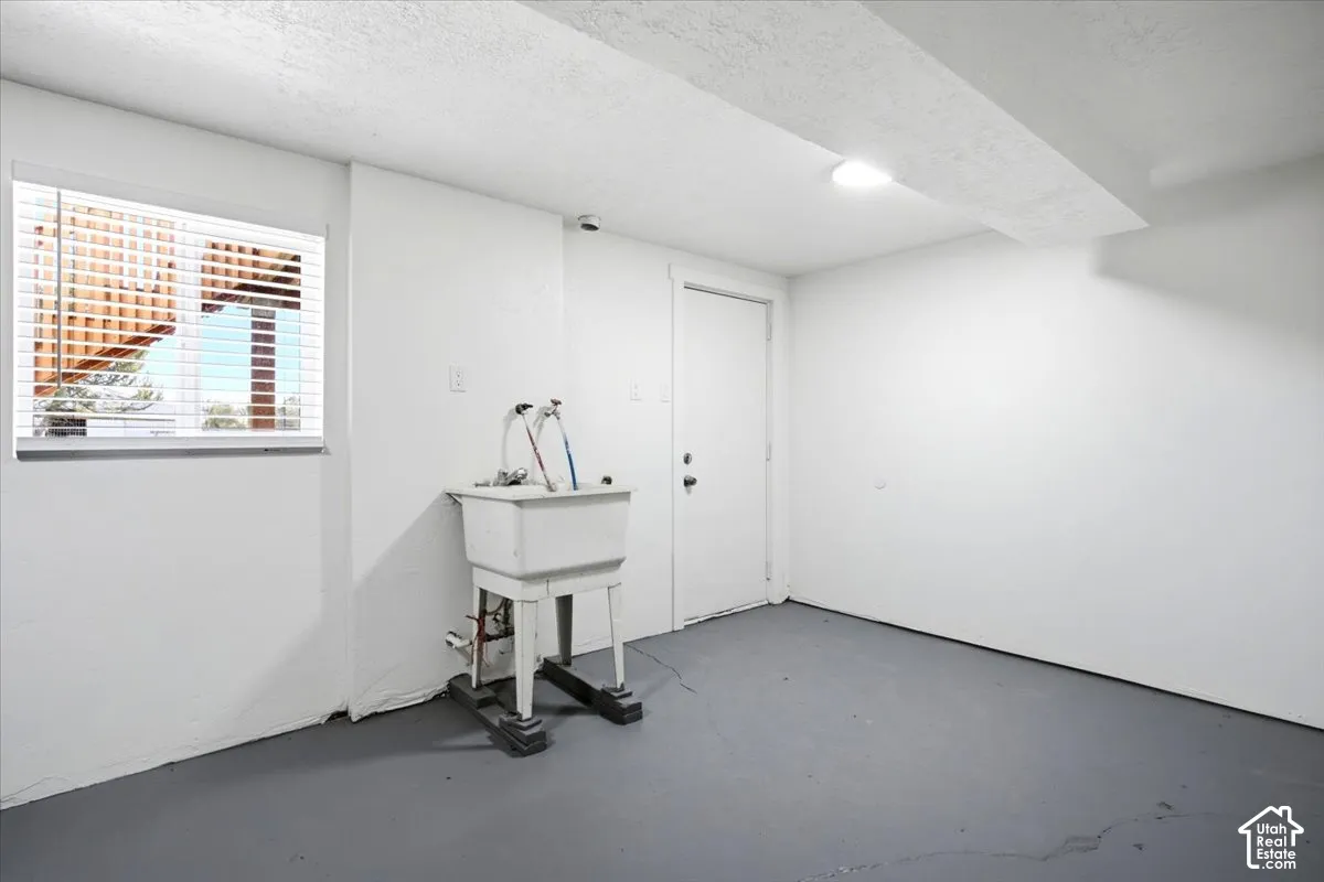 Utility sink with exposed plumbing, window with horizontal blinds, and a white interior door