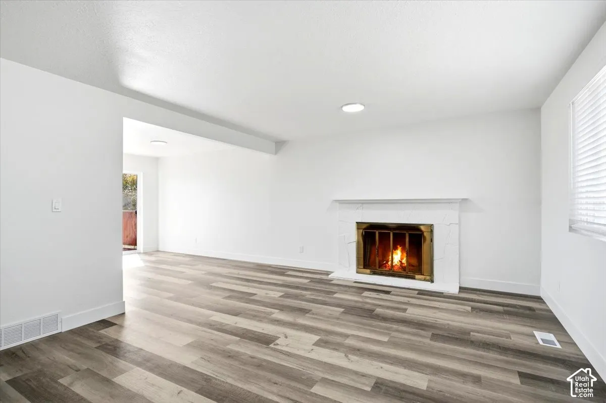 Wood-finish flooring, white walls, and a white fireplace with a brass insert