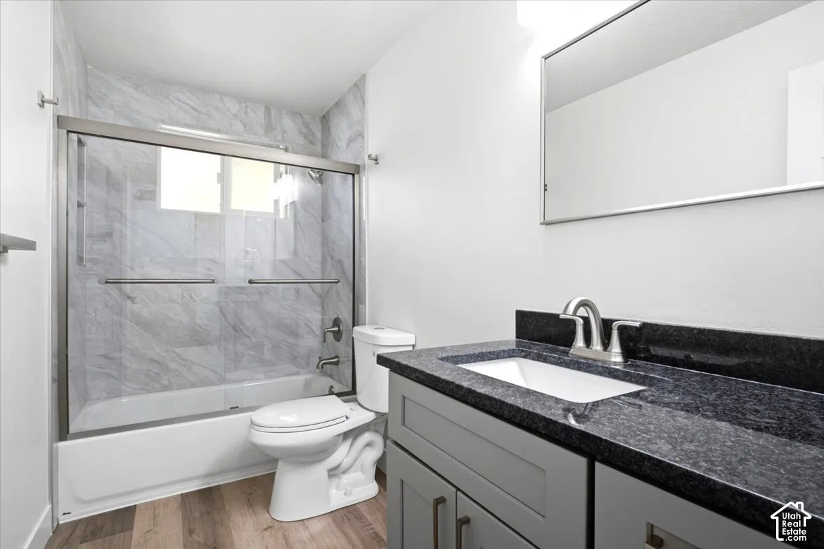 White wall paint, gray vanity, dark stone-finish countertop, stainless steel sink faucet, and wood-finish flooring