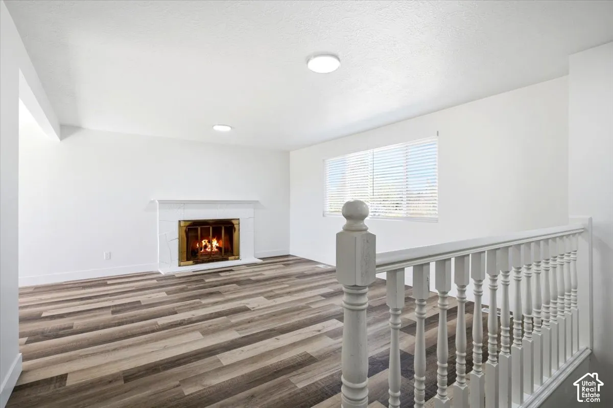 Wood-finish flooring, white walls, and a fireplace with a white mantel and brass-tone insert