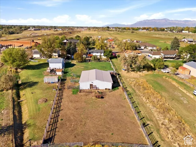 Expansive property featuring a large metal-sided building, fenced outdoor areas, and distant mountainous terrain