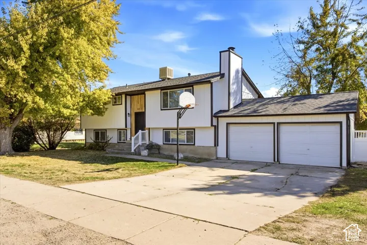 Split-level residence featuring a two-car garage, concrete driveway, and established trees