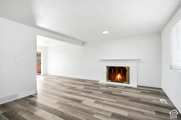 Wood-finish flooring, white walls, and a white fireplace with a brass insert