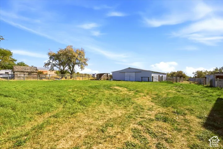 Expansive grassy area with a large metal barn structure, perimeter fencing, and mature trees
