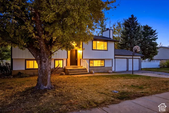 Split-level residence featuring white siding with dark trim, a two-car garage, and concrete steps to the main entry
