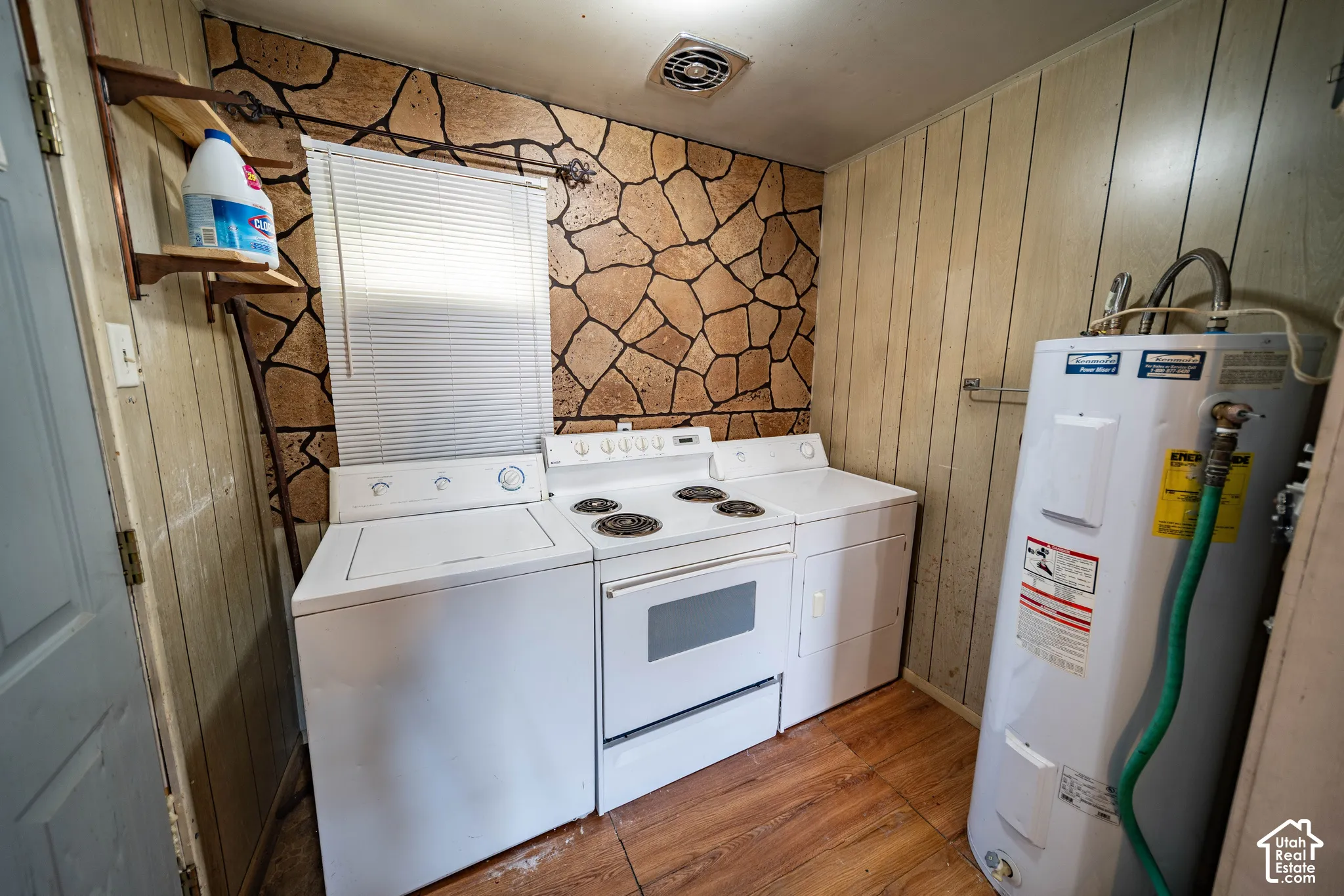 Laundry area with wood-finish flooring, stone-finish wall, and a built-in water heater