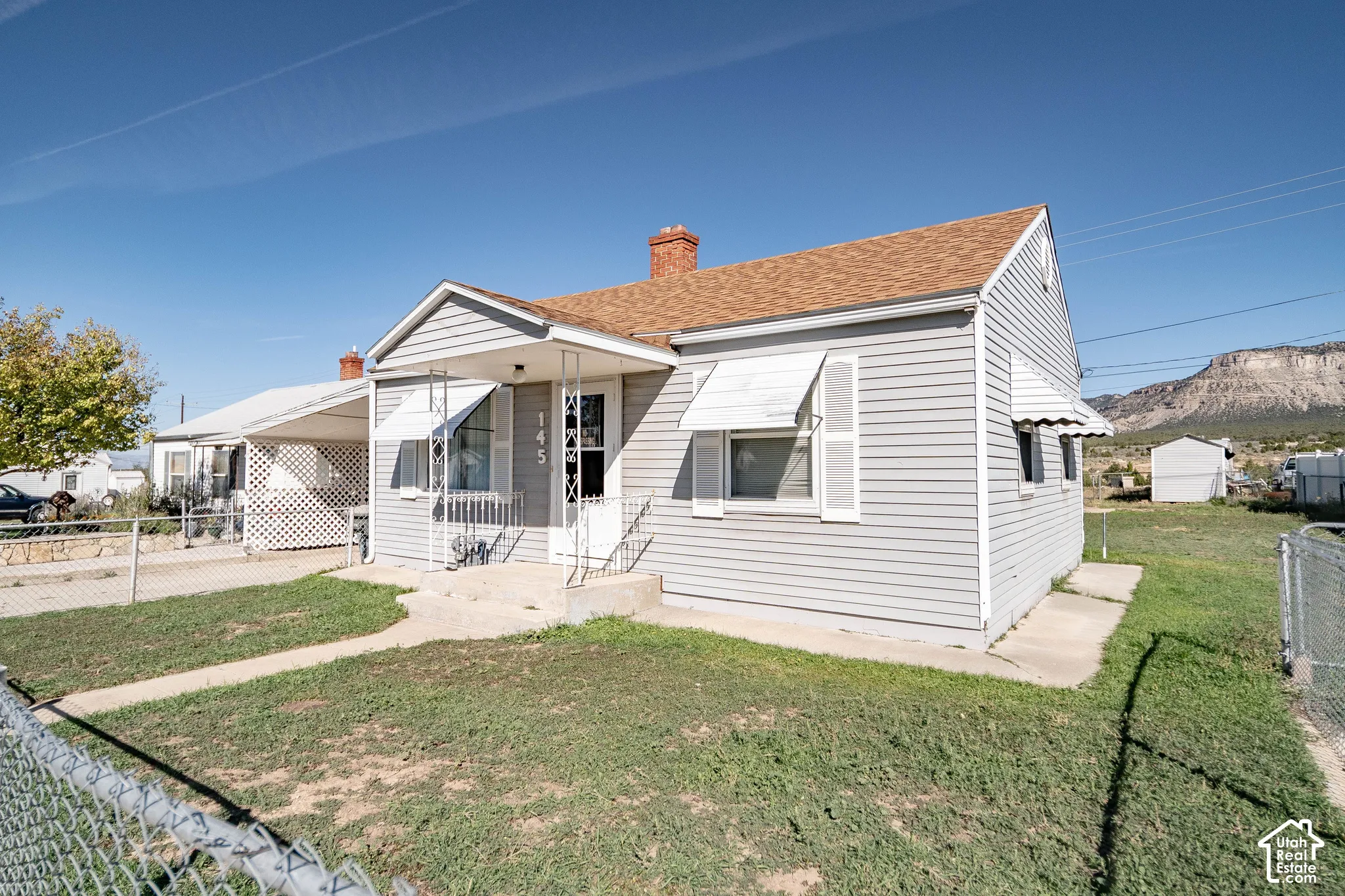 Light gray siding exterior with white window awnings, a front porch with white metal railings, and a brown shingle roof