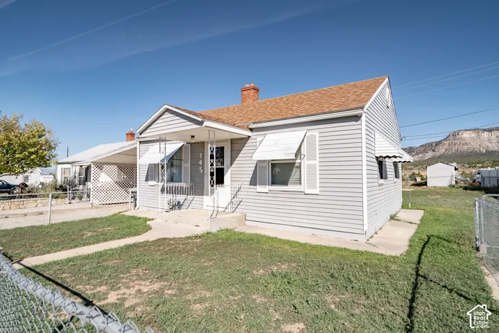 Light gray siding exterior with white window awnings, a front porch with white metal railings, and a brown shingle roof
