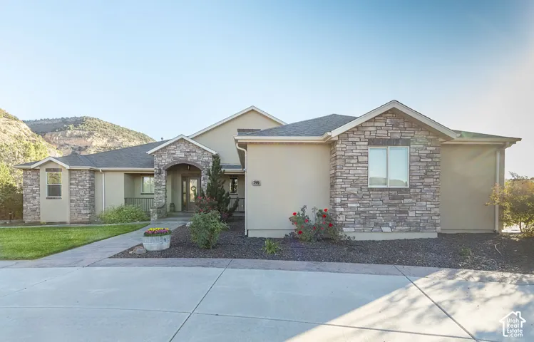 Stucco exterior with stone accents, covered entry, front concrete walkway, and landscaped garden beds