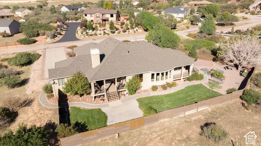Expansive asphalt driveway, concrete patio, fenced backyard, manicured lawn, and raised garden beds