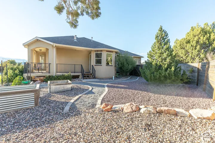 Elevated rear patio with black metal railing, stucco exterior, multiple window styles, gravel landscaping, and a privacy fence