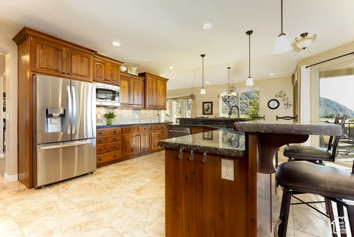 Kitchen featuring stainless steel appliances, wood cabinetry, stone countertops, and tile flooring