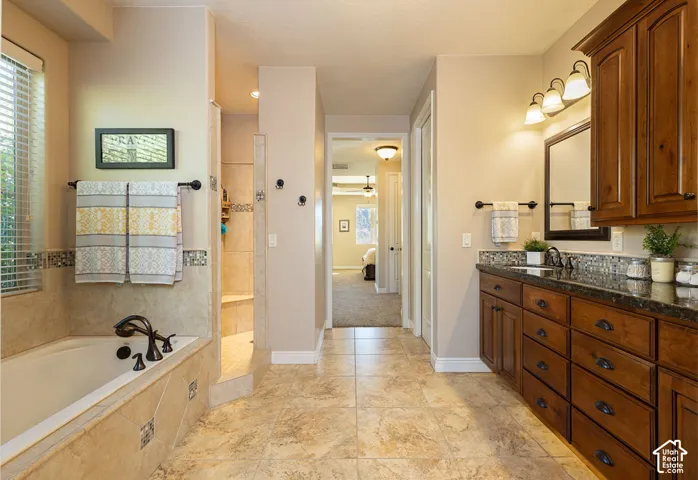 Tiled flooring, built-in soaking tub, walk-in shower, rich wood-finish vanity with countertop, and recessed lighting