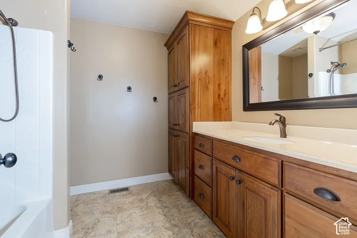 Bathroom featuring a wood-finish vanity with an integrated sink, a large framed mirror, and a full-height wood-finish storage cabinet