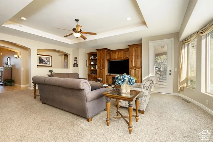 Tray ceiling with recessed lighting, integrated ceiling fan, built-in entertainment center with wood cabinetry, arched doorways, and a full-light exterior door
