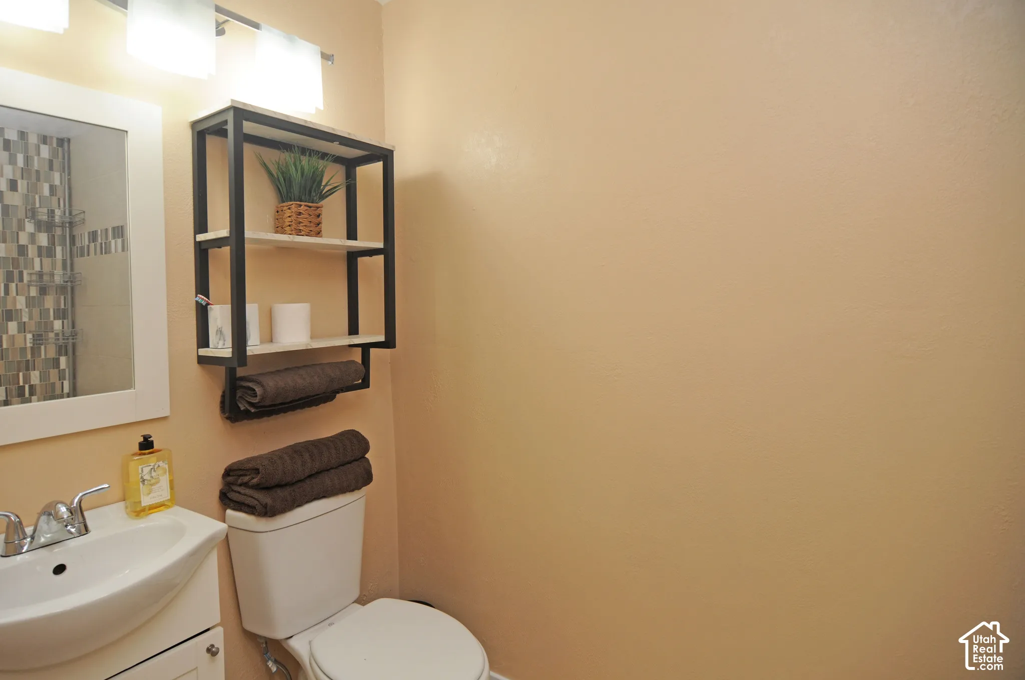 White vanity with a ceramic sink, chrome faucet, and overhead three-bulb vanity light