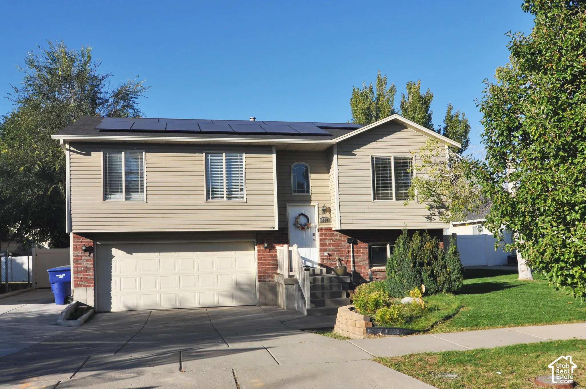 Siding exterior with brick accents, attached two-car garage, front walk-up entry, mature landscaping, and rooftop solar panels