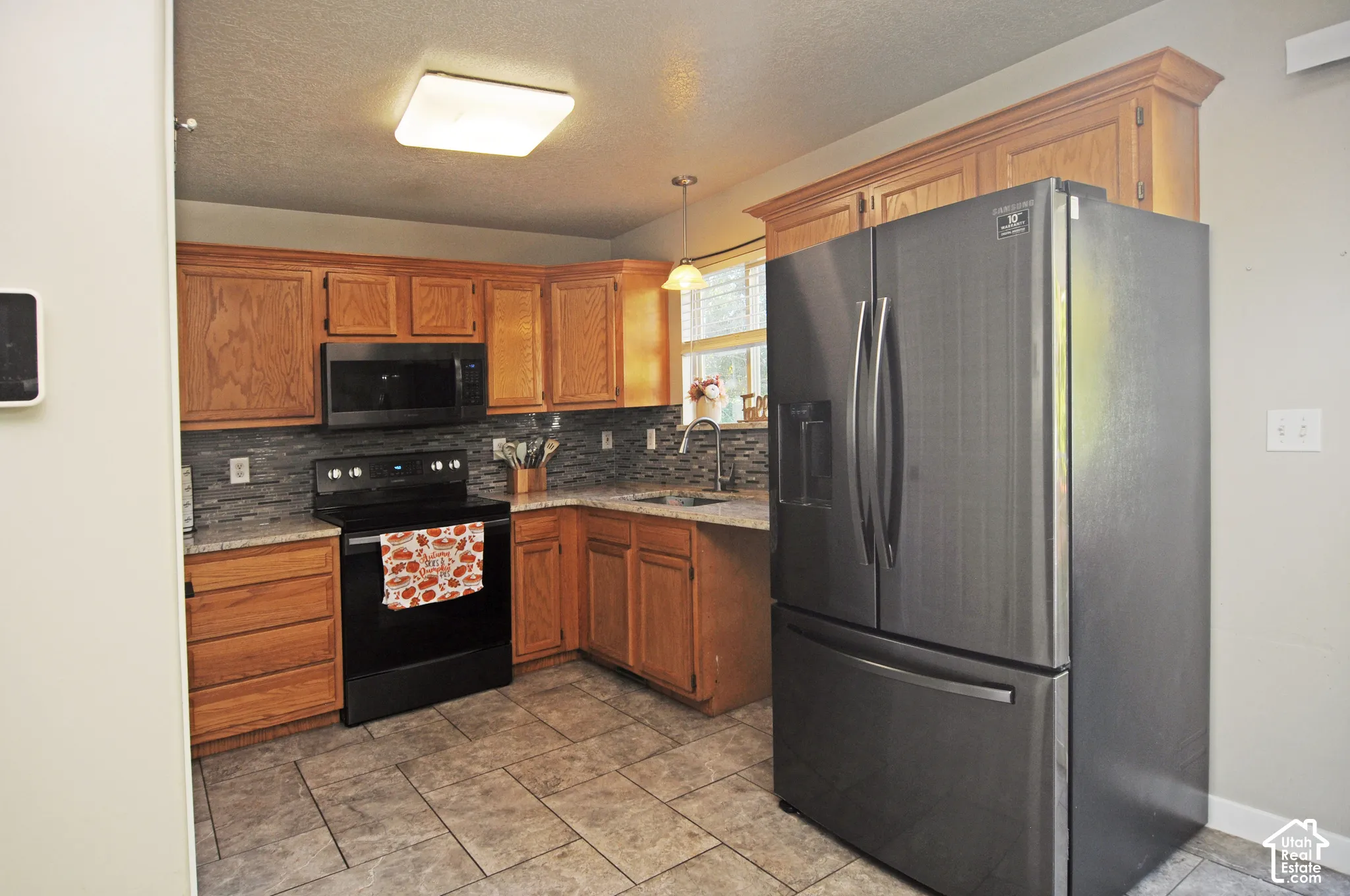 Kitchen featuring wood cabinetry, a dark tile backsplash, light-toned countertops, and stainless steel appliances