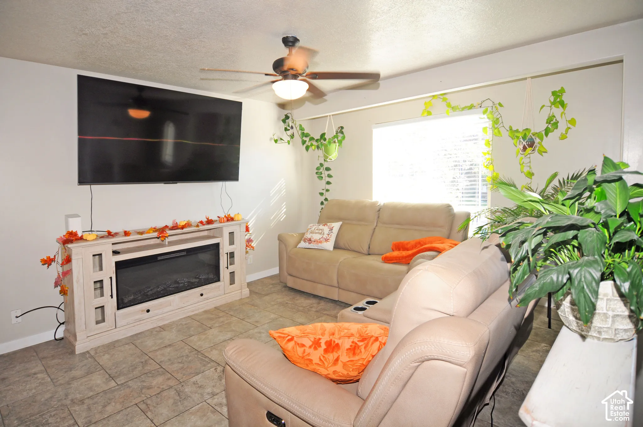 Tiled flooring, ceiling fan with integrated lighting, built-in entertainment console with electric fireplace, and window with horizontal blinds