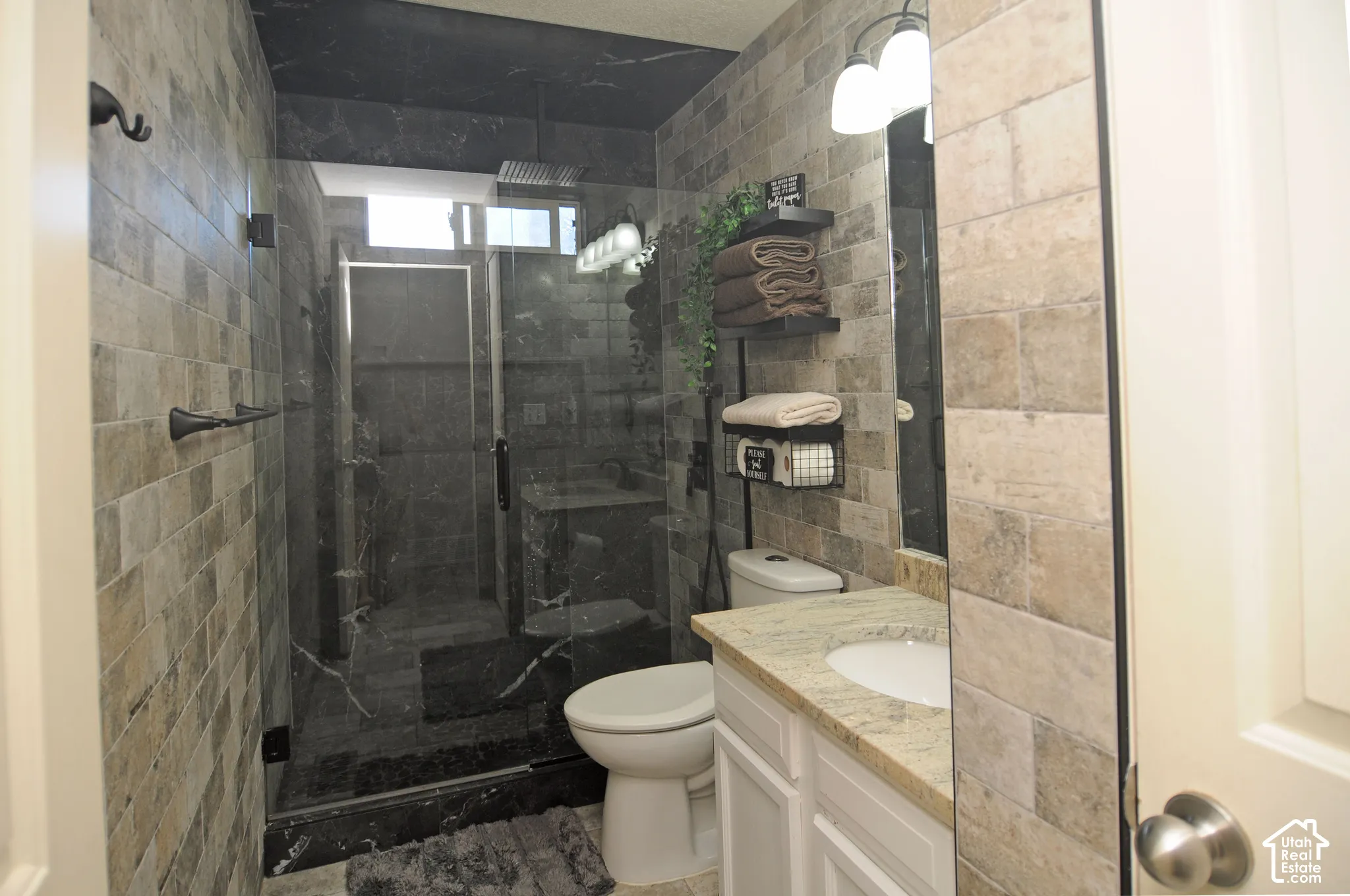 Walk-in shower with clear glass enclosure, black marble-look tile, rainfall showerhead, and transom window