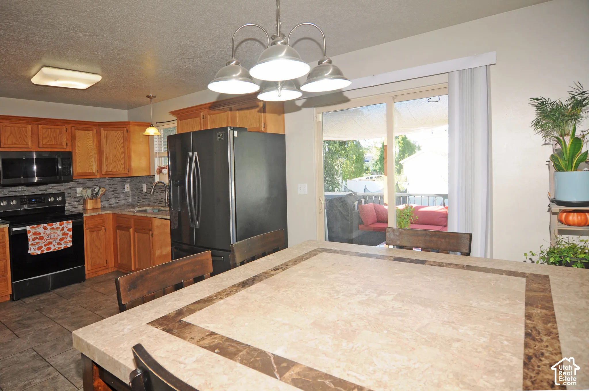 Kitchen featuring wood cabinetry, black appliances, tile backsplash, and a dining counter with an integrated stone-finish top