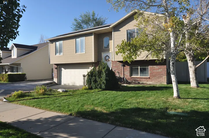 Two-story residence featuring tan siding, a brick facade, and an attached two-car garage