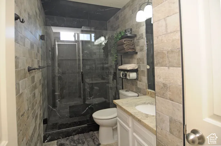 Walk-in shower with clear glass enclosure, black marble-look tile, rainfall showerhead, and transom window