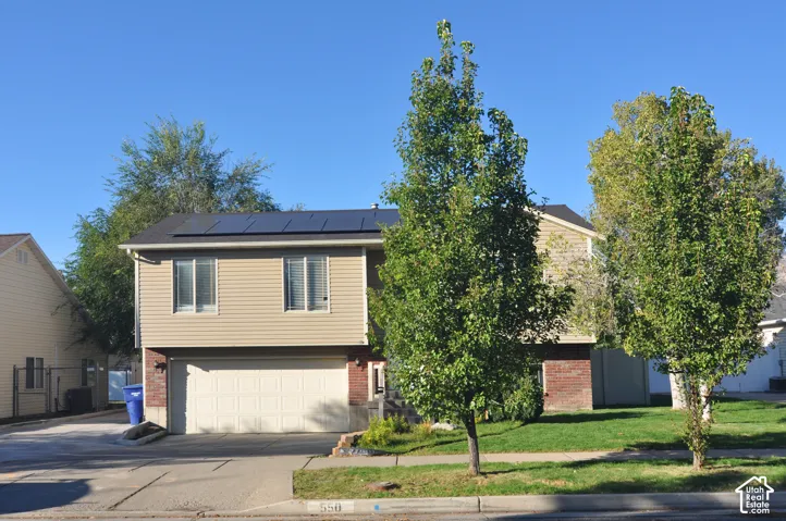 Split-level residence featuring a two-car garage, solar panels, and a combination of brick and siding exterior
