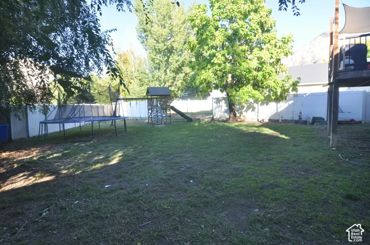 Expansive fenced yard with a manicured lawn, mature trees, and a raised wooden deck
