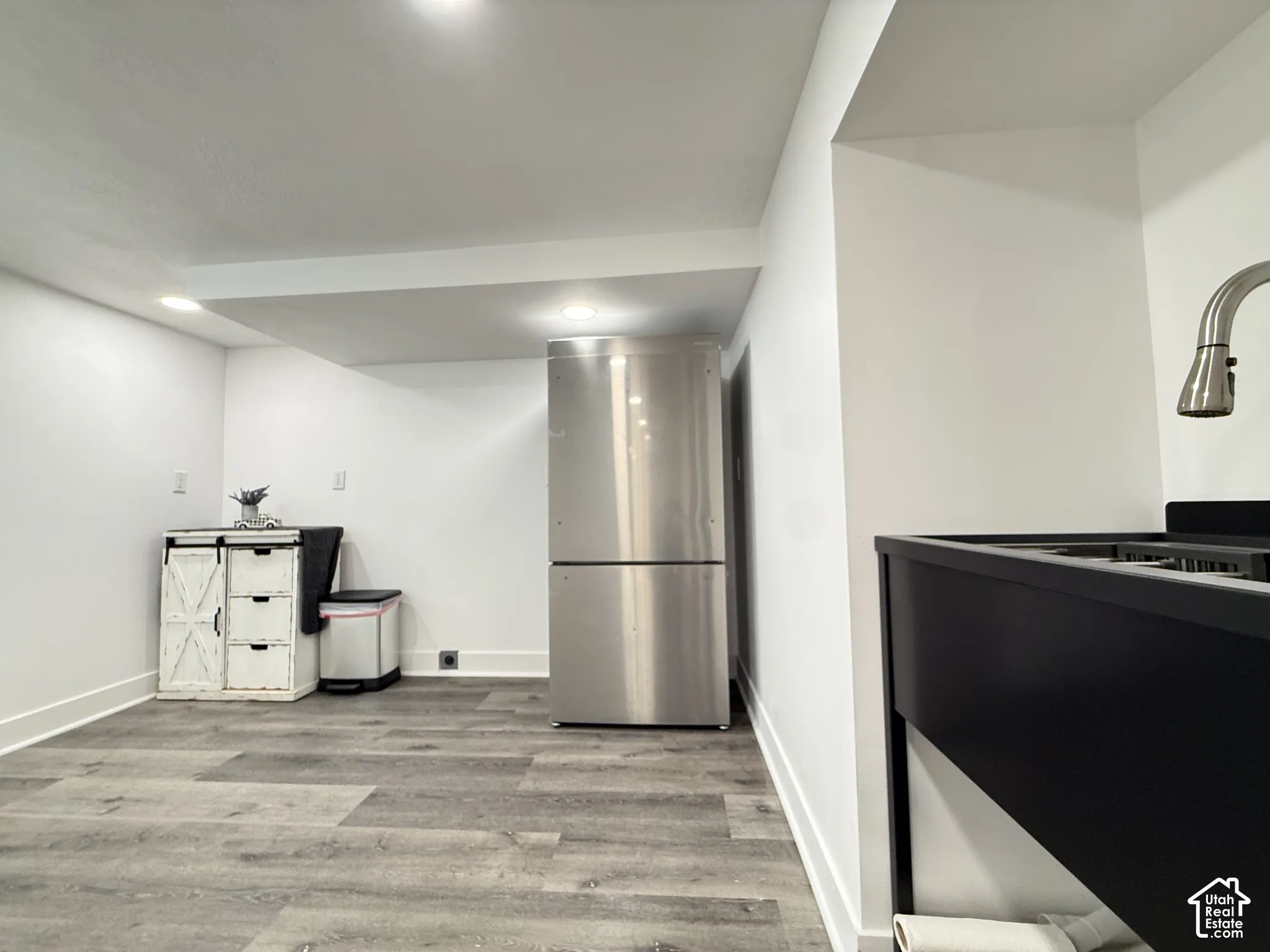 Stainless steel refrigerator, wood-finish flooring, and black matte utility sink with a high-arch faucet