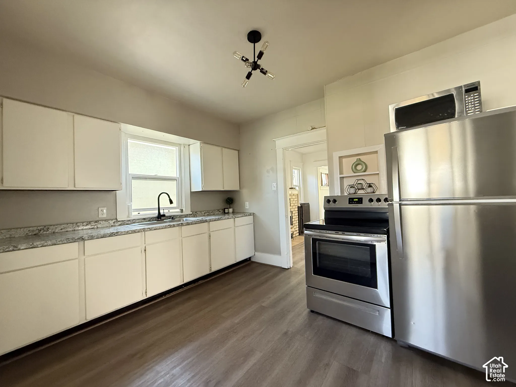 Kitchen featuring white cabinetry, stone-patterned countertops, stainless steel appliances, wood-finish flooring, and a multi-bulb flush-mount light fixture