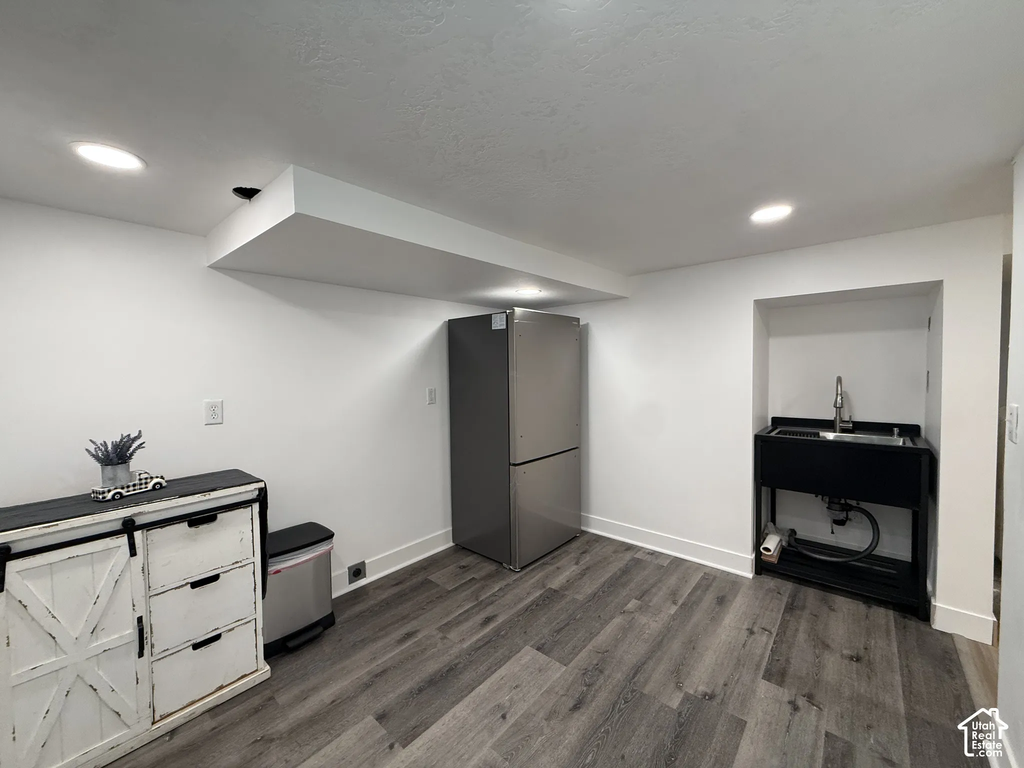 Wood-finish flooring, stainless steel refrigerator, recessed lighting, and a utility sink with a high-arch faucet