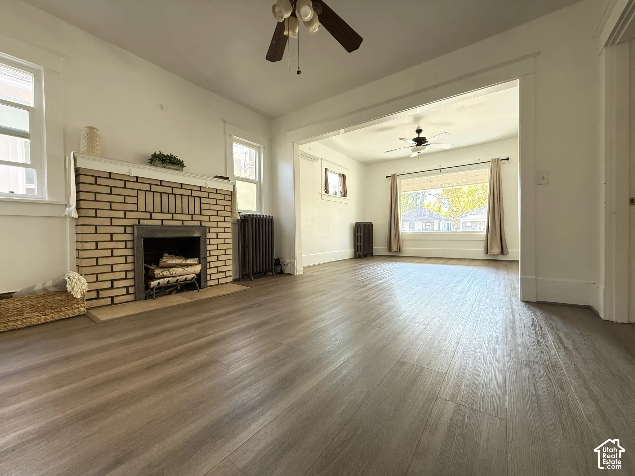 Living area featuring wood-finish flooring, brick fireplace with mantel, ceiling fans, and cast-iron radiators