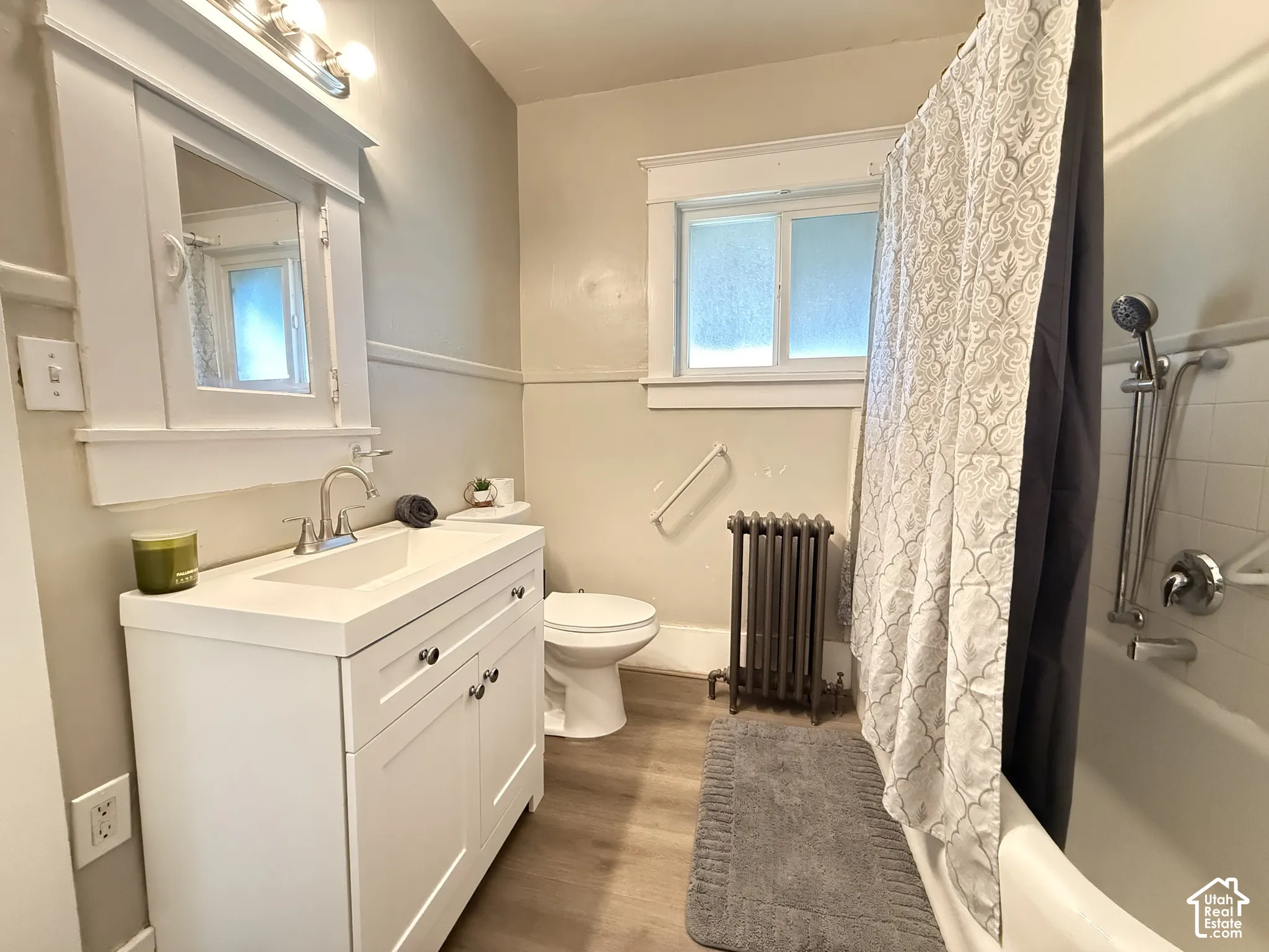 Bathroom featuring a white vanity with an integrated rectangular sink, built-in medicine cabinet with mirror, wall-mounted cast iron radiator, and wood-finish flooring