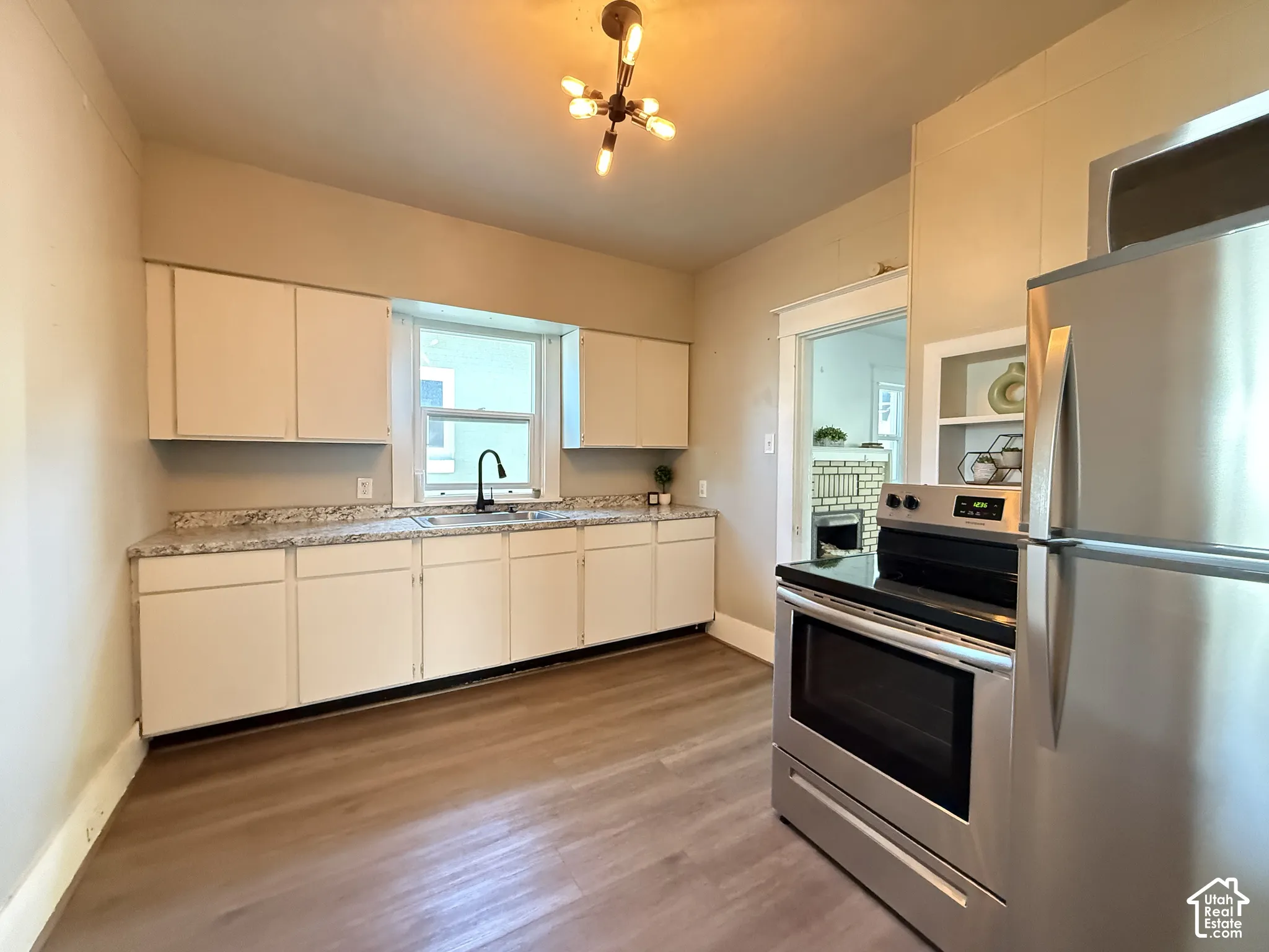 Kitchen featuring matte white cabinetry, stone-patterned countertops, stainless steel appliances, wood-finish flooring, and a multi-bulb industrial style ceiling fixture