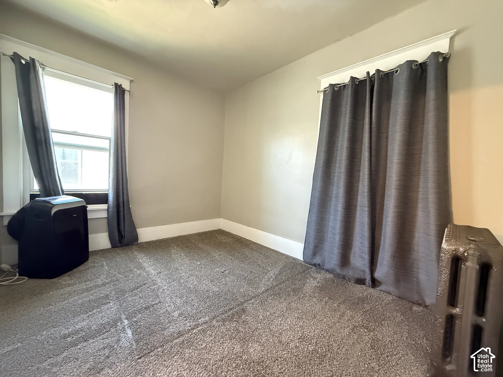 Interior room featuring neutral wall paint, wall-to-wall carpeting, window casing with sash windows, and an original cast-iron radiator