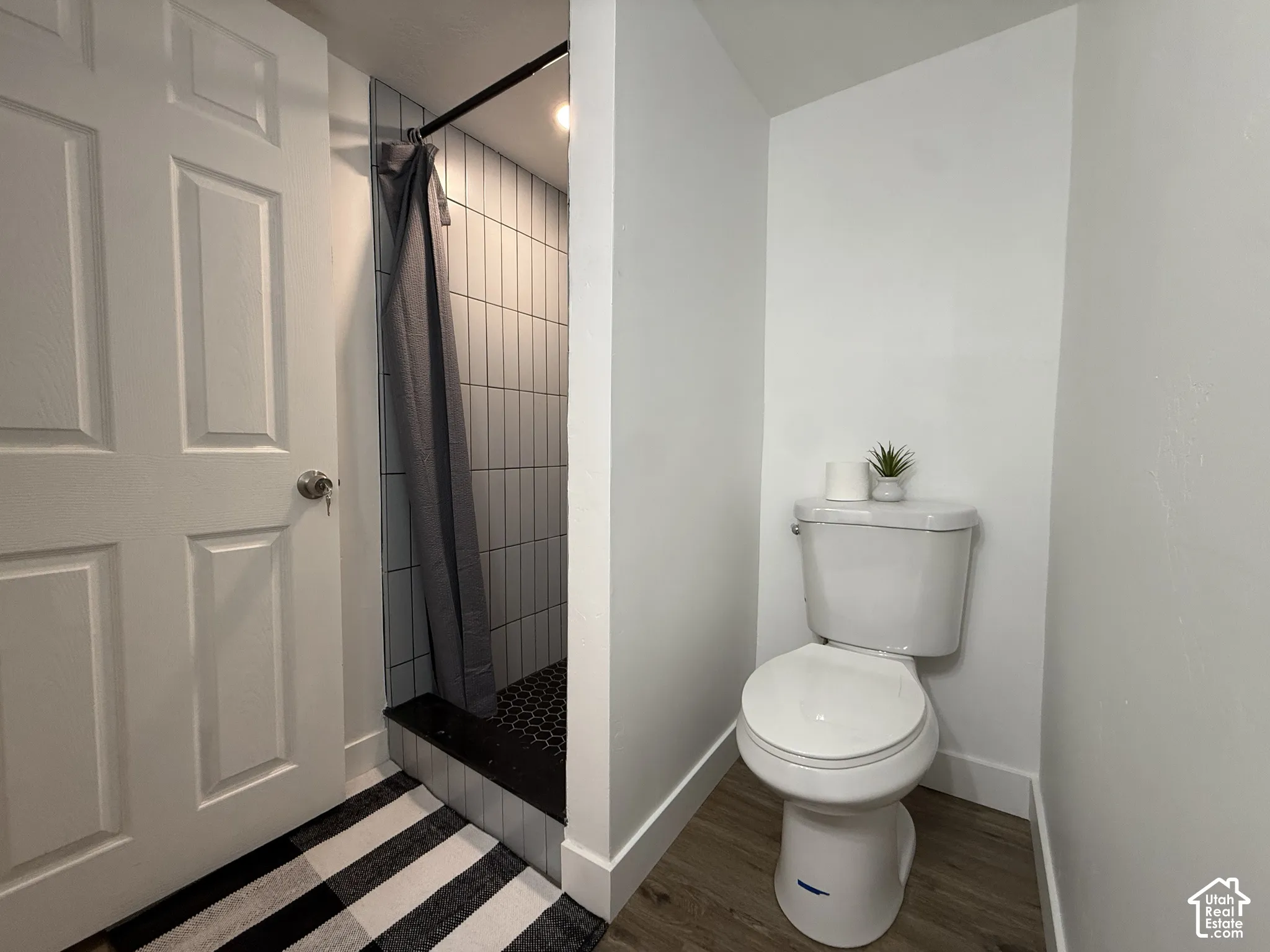Bathroom featuring a walk-in shower with vertical wall tiling and dark hexagonal floor tile, complemented by wood-finish flooring and a white two-piece toilet